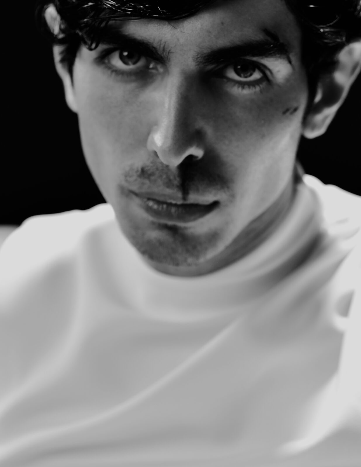 Black-and-white close portrait of a young man in a white top — Abdullah Al Zanki for ZELZAL