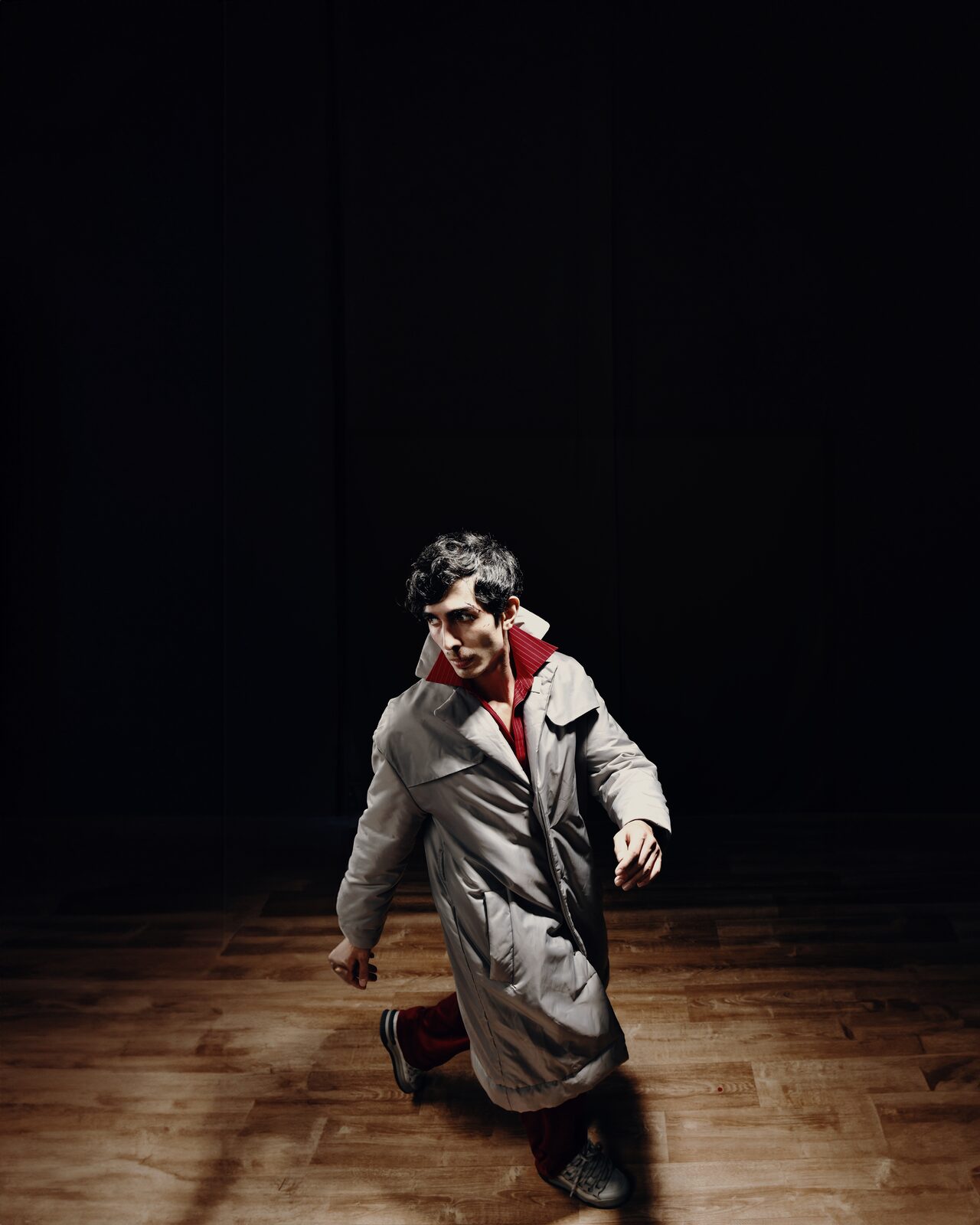 Man with face markings in a long grey coat on a wooden stage floor — Abdullah Al Zanki for ZELZAL
