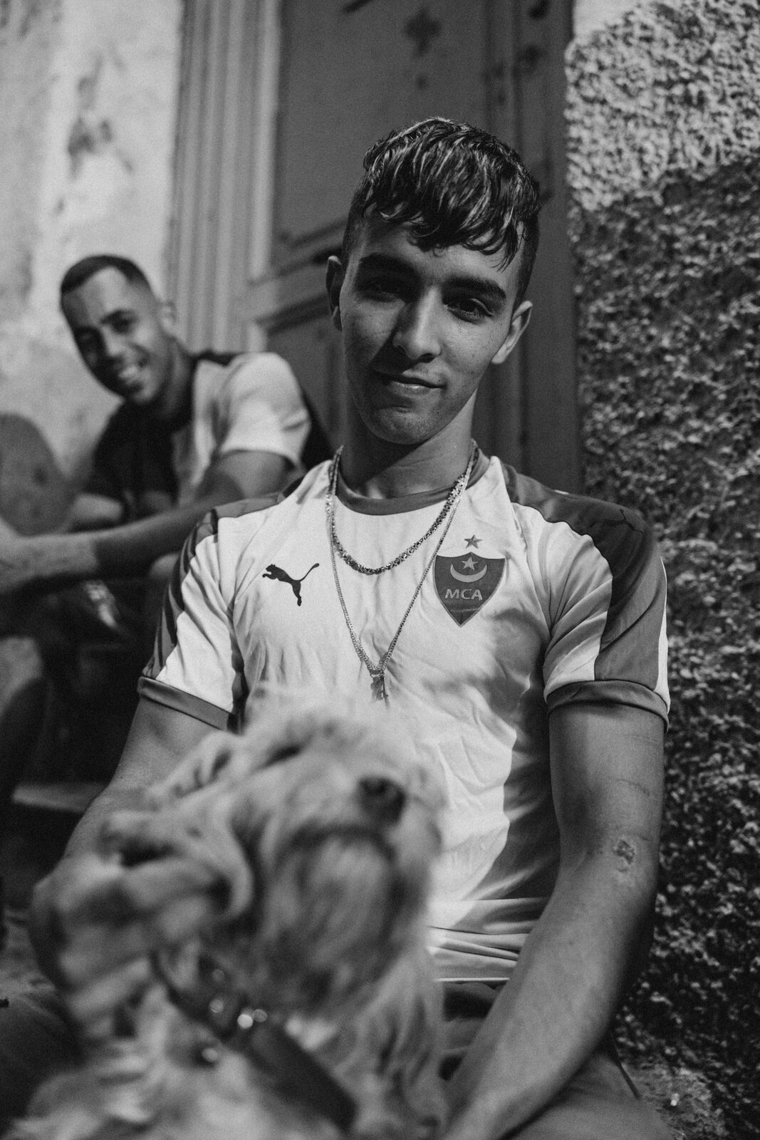 Black-and-white portrait of a young man in a football shirt with a dog — Aqib Anwar for ZELZAL