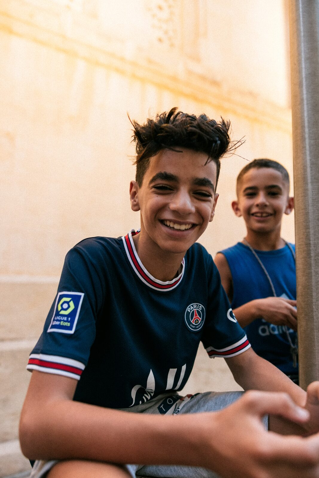 Two smiling boys, one in a PSG shirt, at golden hour — Aqib Anwar for ZELZAL