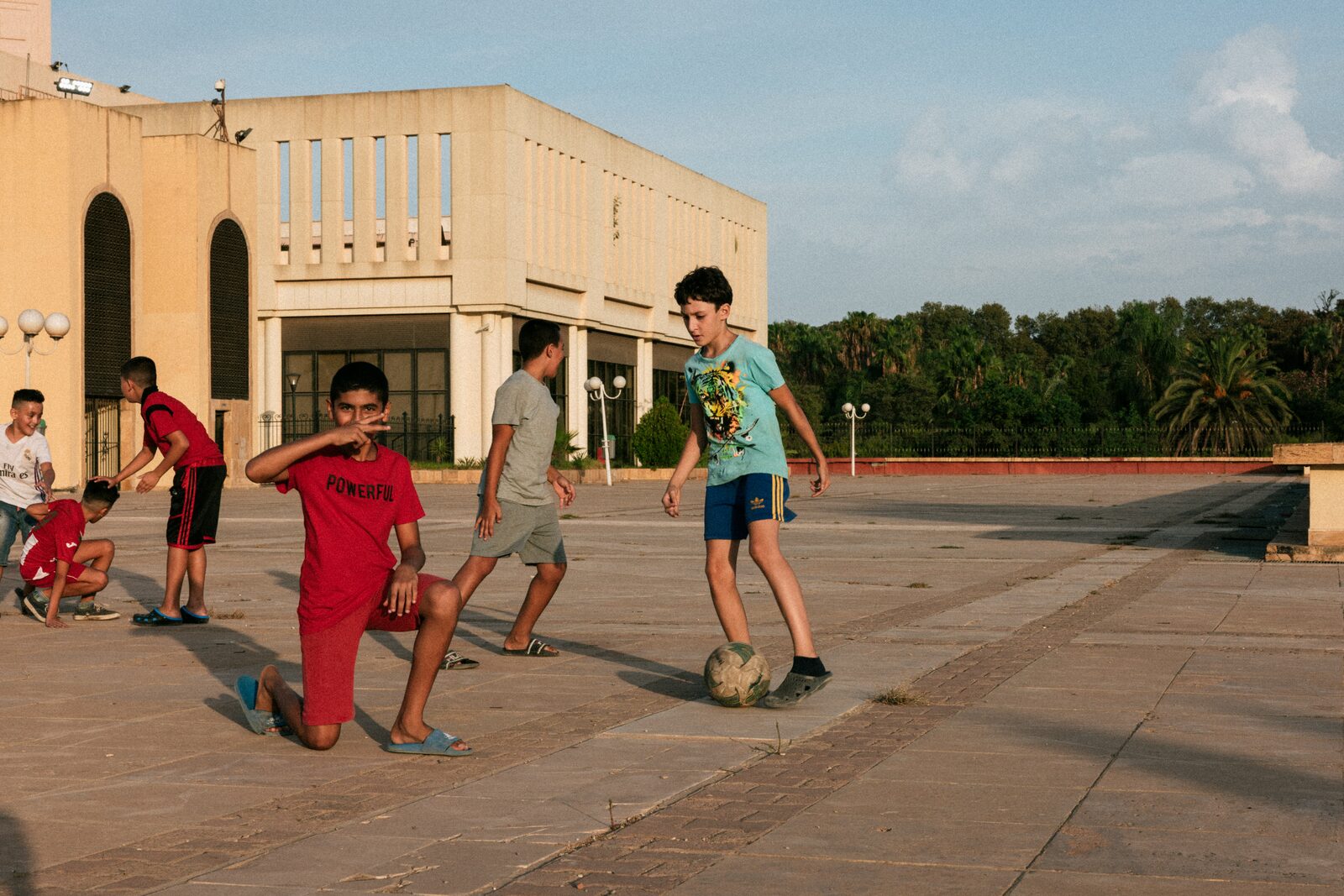 Boys playing football on a square in front of a beige building — Aqib Anwar for ZELZAL