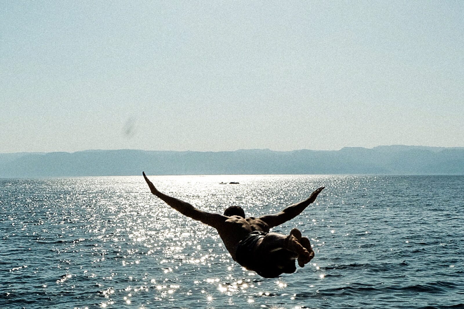 Man diving into a glittering sea, mountains on the horizon — Baha Suleiman for ZELZAL