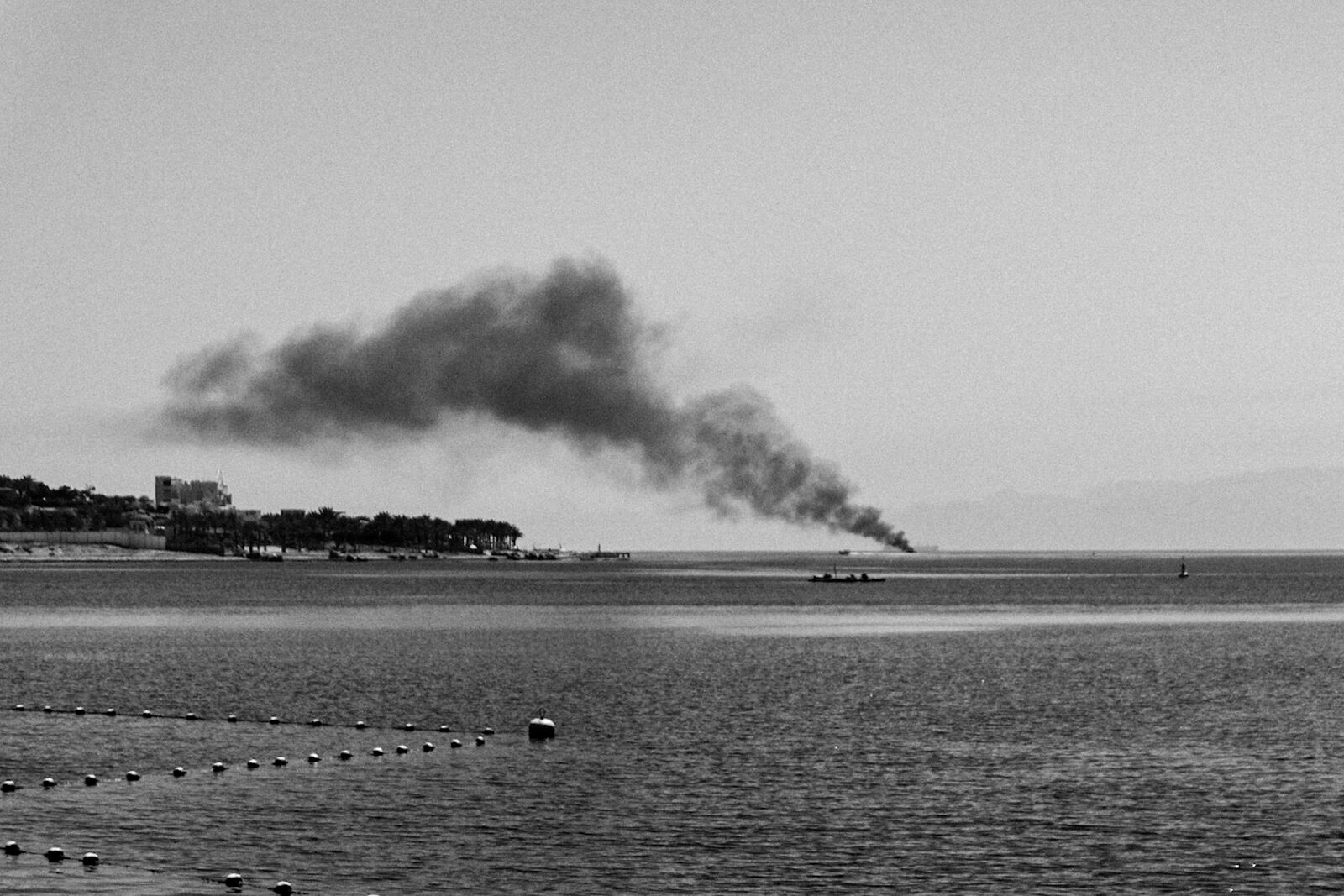 Black-and-white seascape with a plume of smoke on the horizon — Baha Suleiman for ZELZAL