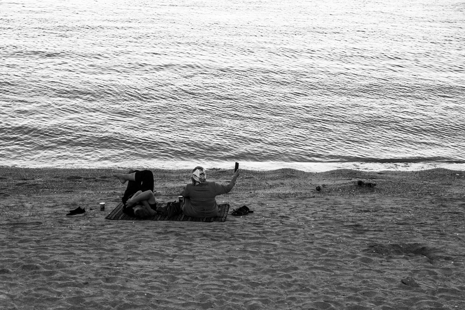 Black-and-white figure lying on a beach by the waves — Baha Suleiman for ZELZAL