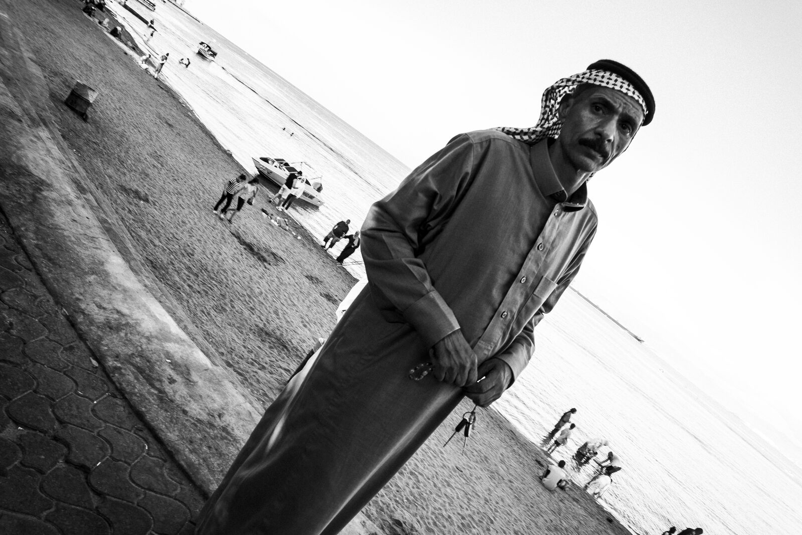 Tilted black-and-white portrait of a man in a keffiyeh on the seafront — Baha Suleiman for ZELZAL