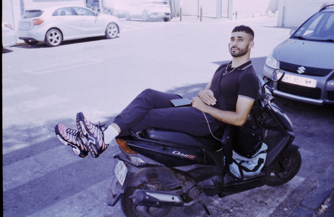 Young man leaning back on a scooter in a street — Basel Hassan for ZELZAL