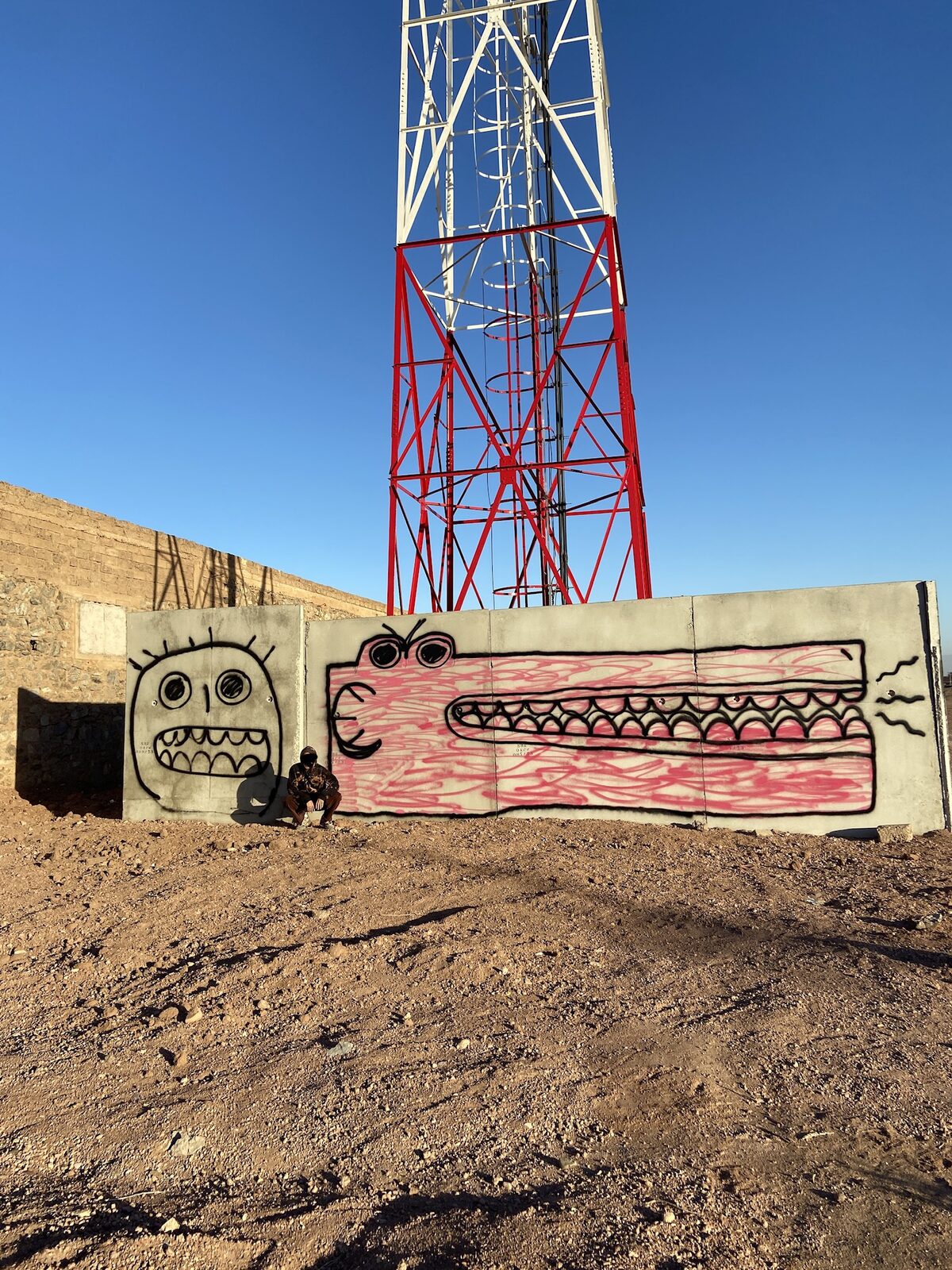 Monster graffiti on a wall below a red-and-white telecom tower — Bluuecrab for ZELZAL