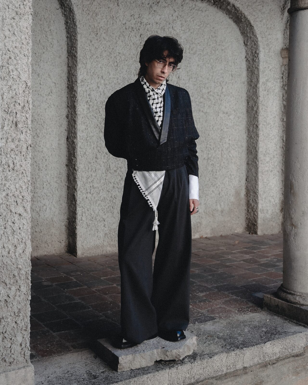 Full-length portrait in wide trousers and keffiyeh scarf under an arcade — Deza for ZELZAL