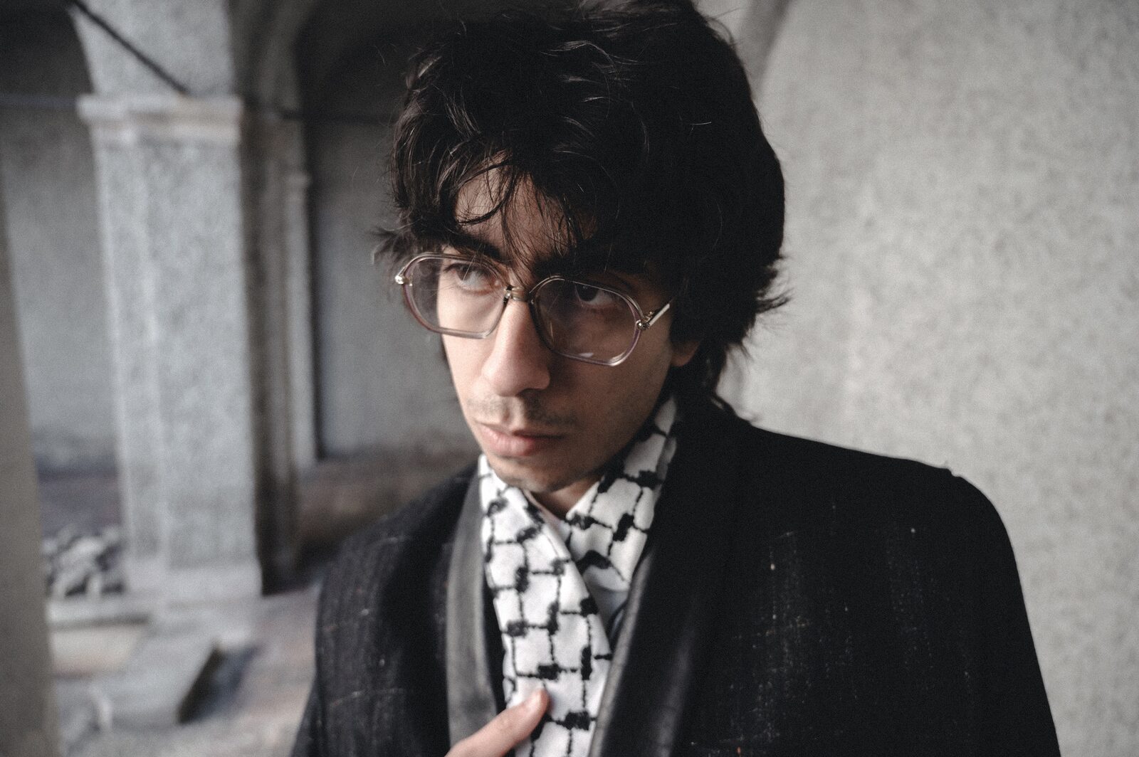 Young man in glasses looking down, keffiyeh around his neck — Deza for ZELZAL