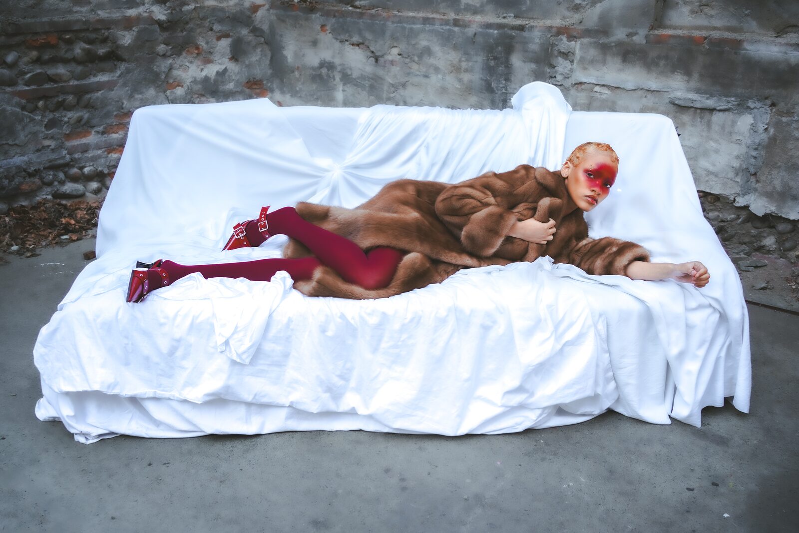 Woman in a fur coat and red boots lying on a white-draped sofa — HunchoSwf / Sawssen Fajr for ZELZAL