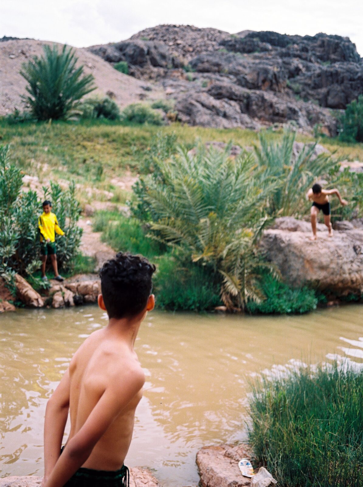 Boy looking at a river among palms and rocks — Ilias El Faris for ZELZAL