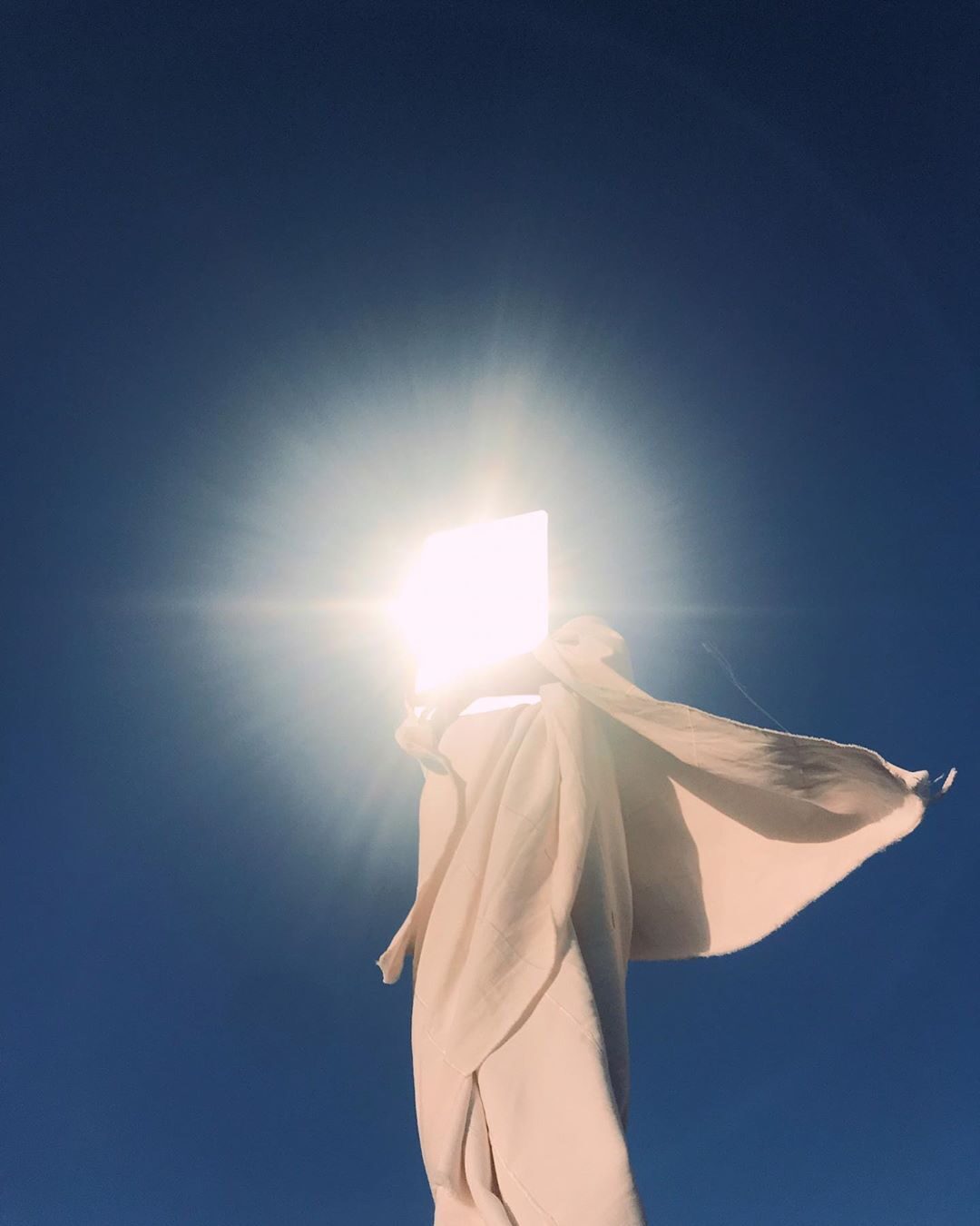 Figure in a beige cape with a bright light for a face against blue — Ismail Zaidy for ZELZAL
