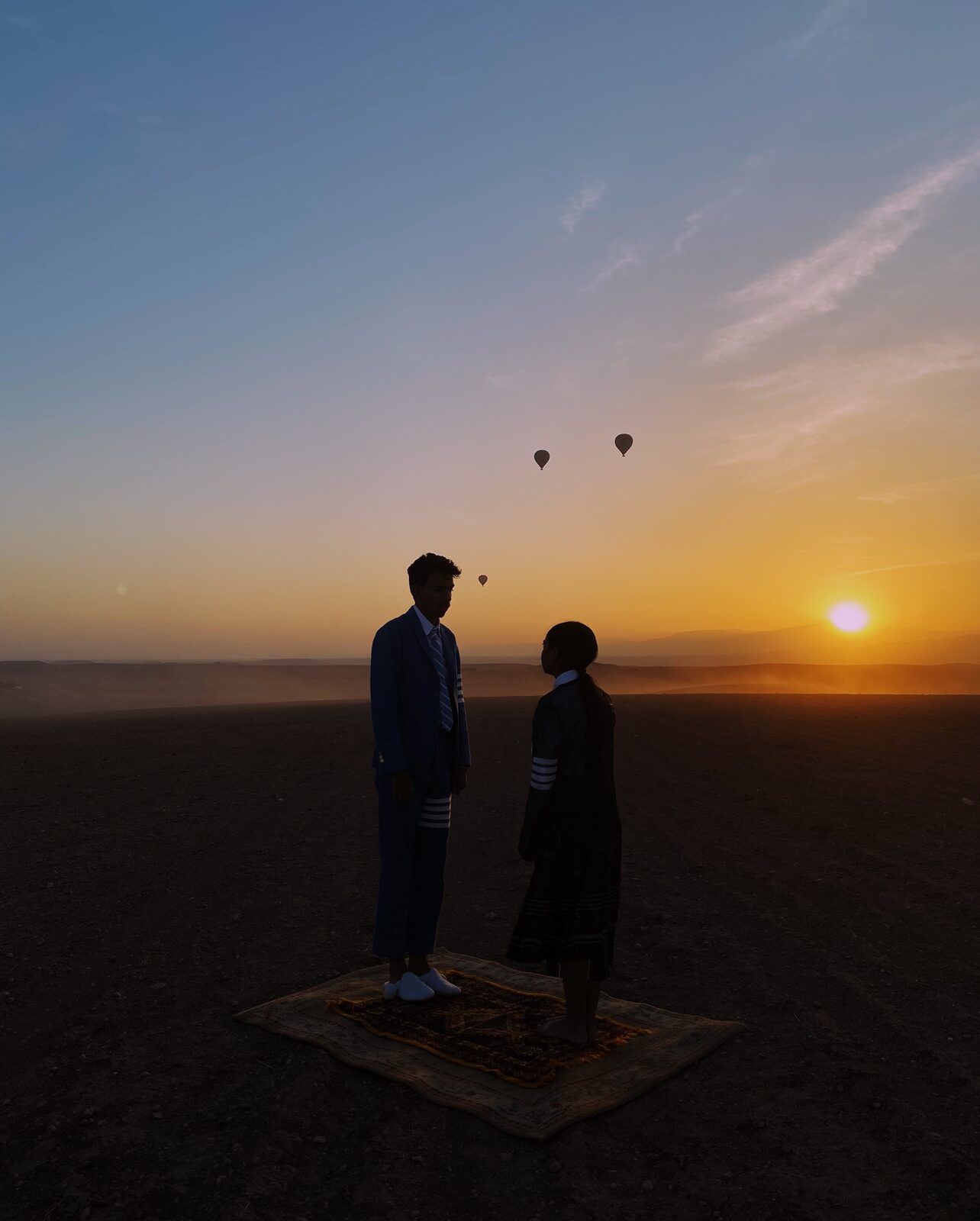 Two figures on a rug in the desert at sunset, balloons in the sky — Ismail Zaidy for ZELZAL