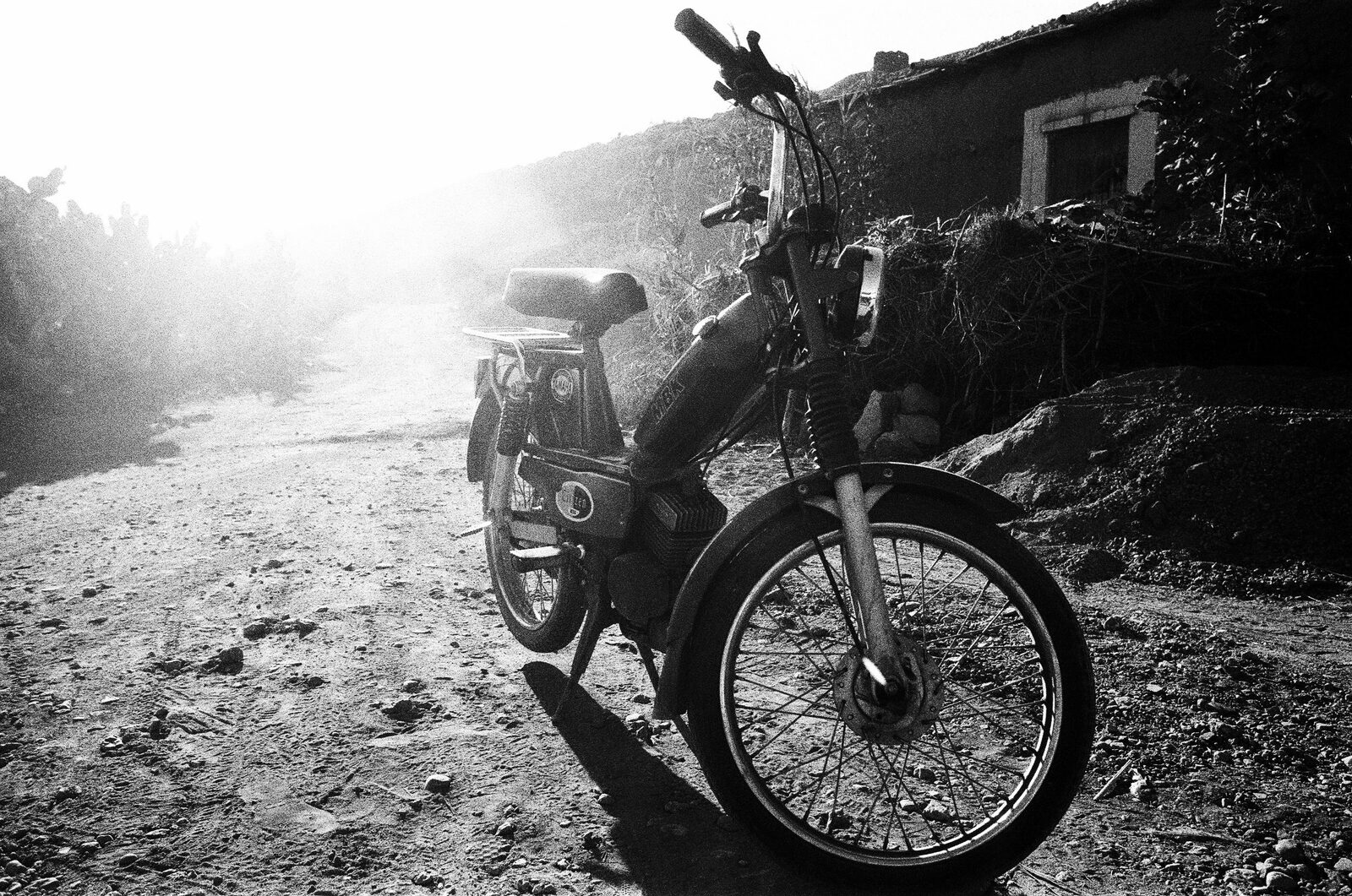 Black-and-white moped on a dirt track against bright light — Lara Perrotte for ZELZAL