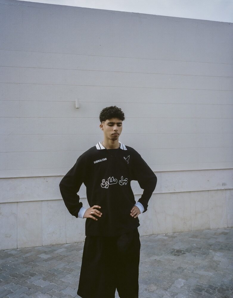 Young man in a black football-style jersey against a white wall — Moz for ZELZAL