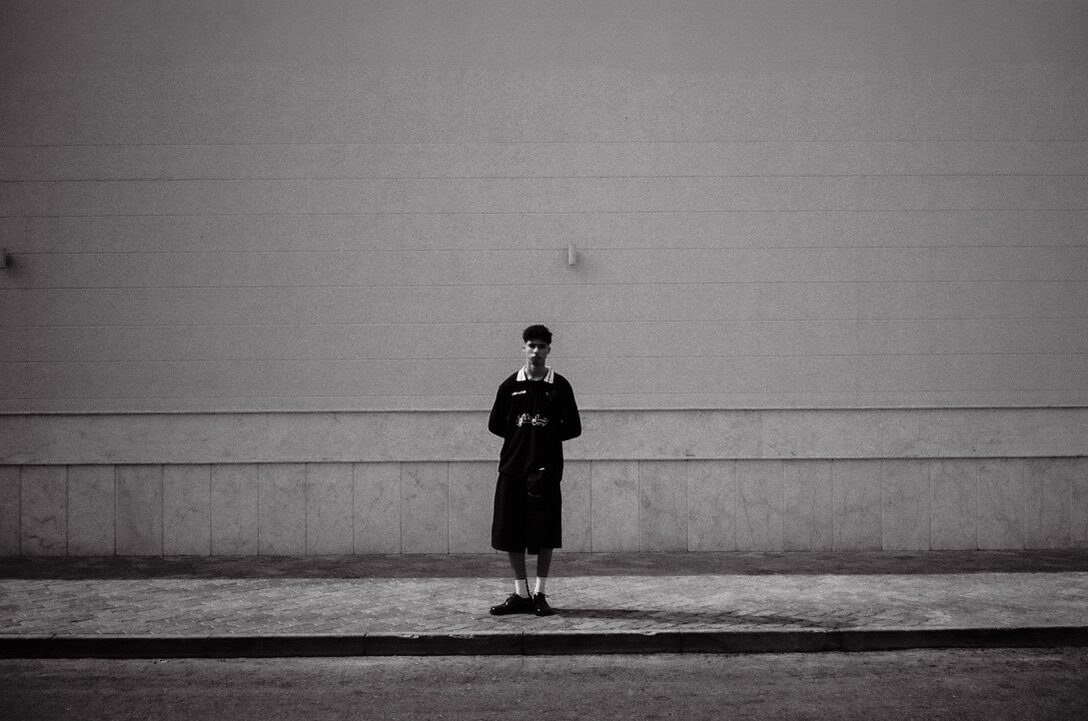 Black-and-white figure standing alone before a long wall — Moz for ZELZAL