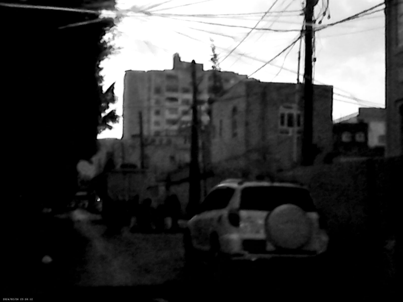Black-and-white street with power lines and a parked car — Sadiq Y. Al-Harasi for ZELZAL