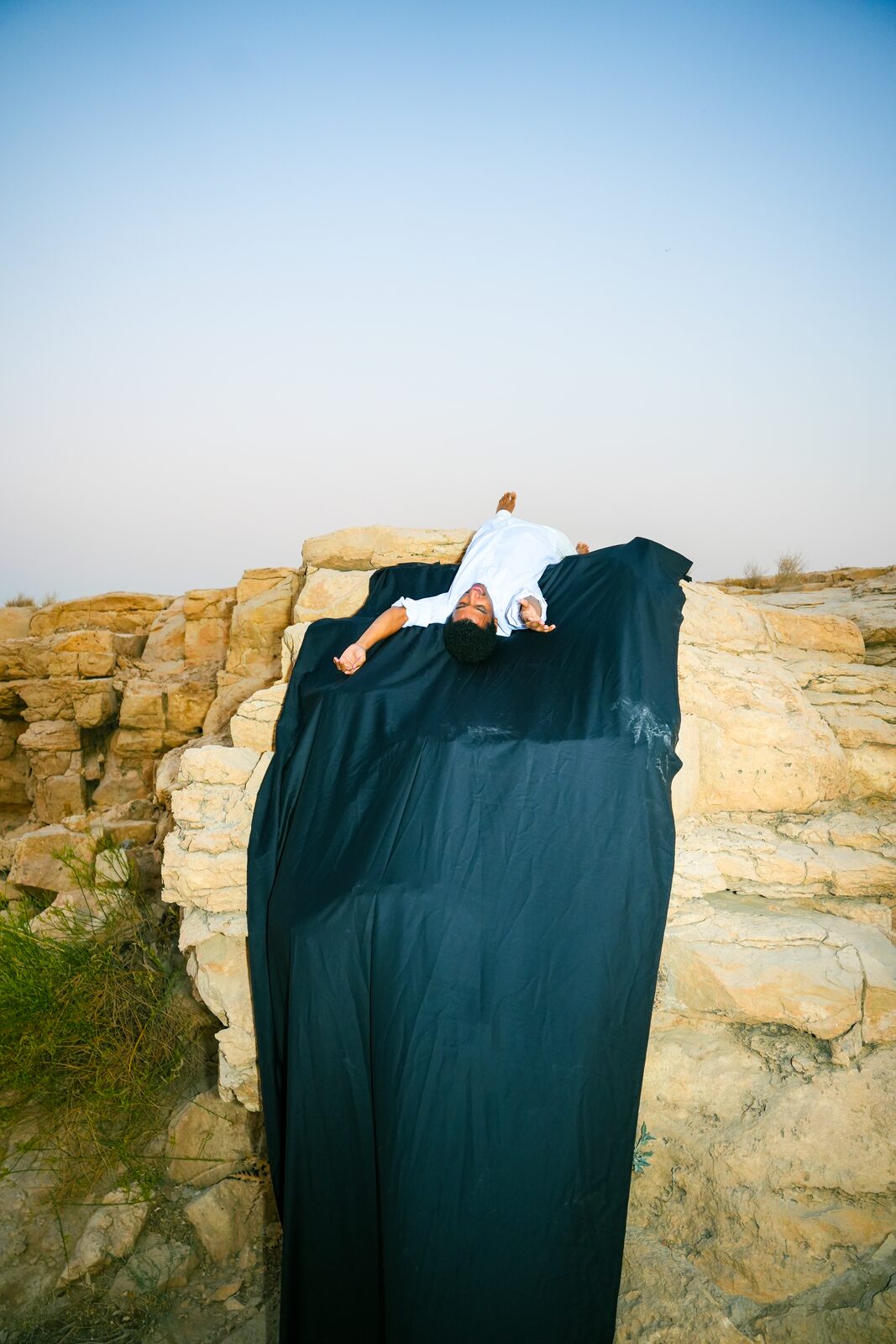 Figure reclining on a cliff with dark fabric cascading down — Salem Hamed Al Shammari (Traceofsalem) for ZELZAL