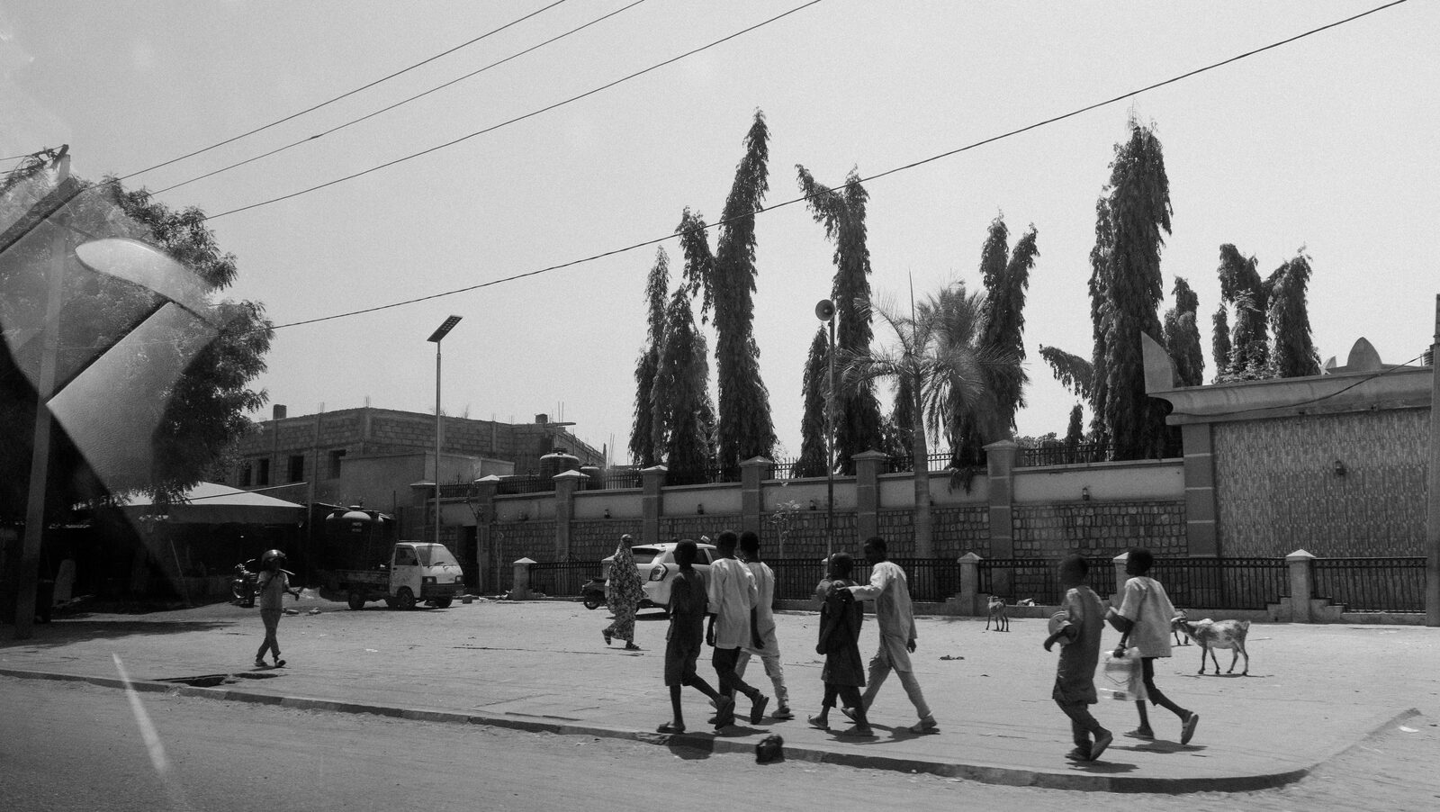 Black-and-white people crossing a road lined with trees — Sumayah Fallatah for ZELZAL
